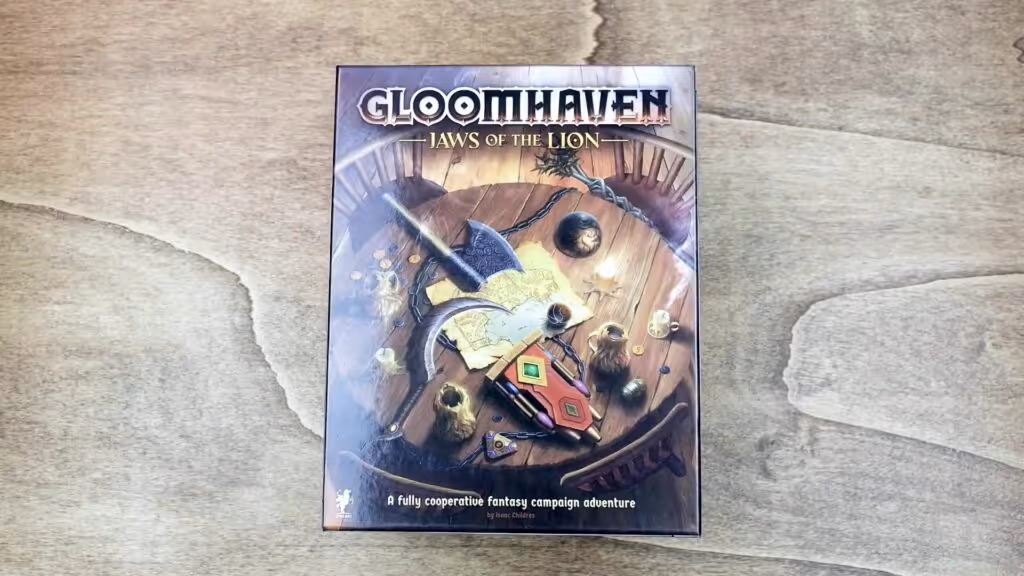 A photograph of the Gloomhaven: Jaws of the Lion board game box, showcasing a detailed illustration of a dungeon scene with characters and a map