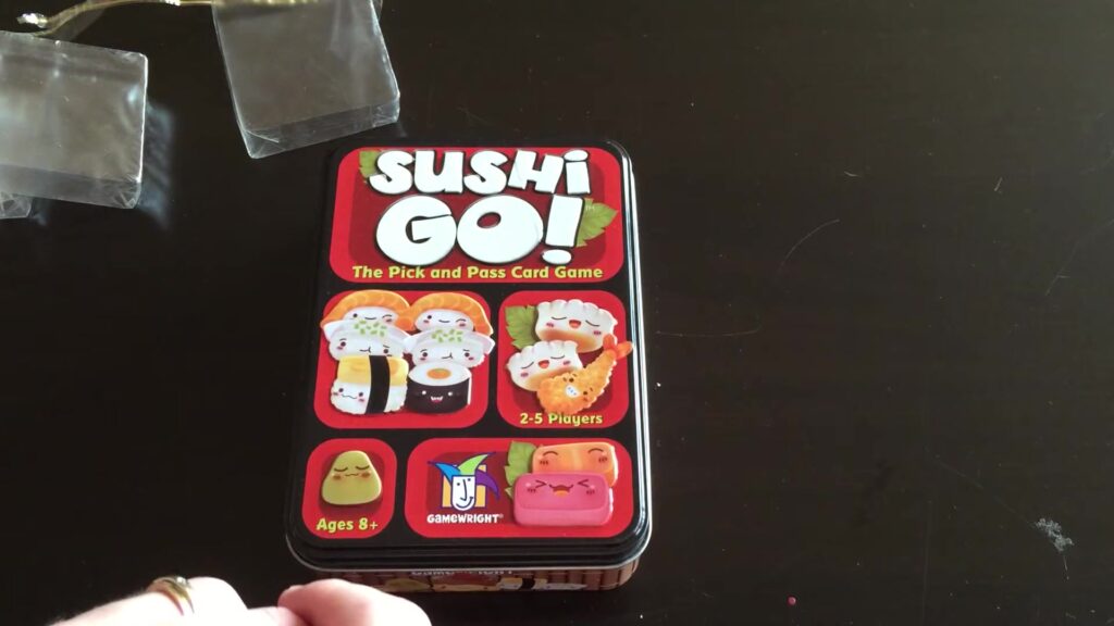Sushi Go card game tin box featuring colorful sushi illustrations.