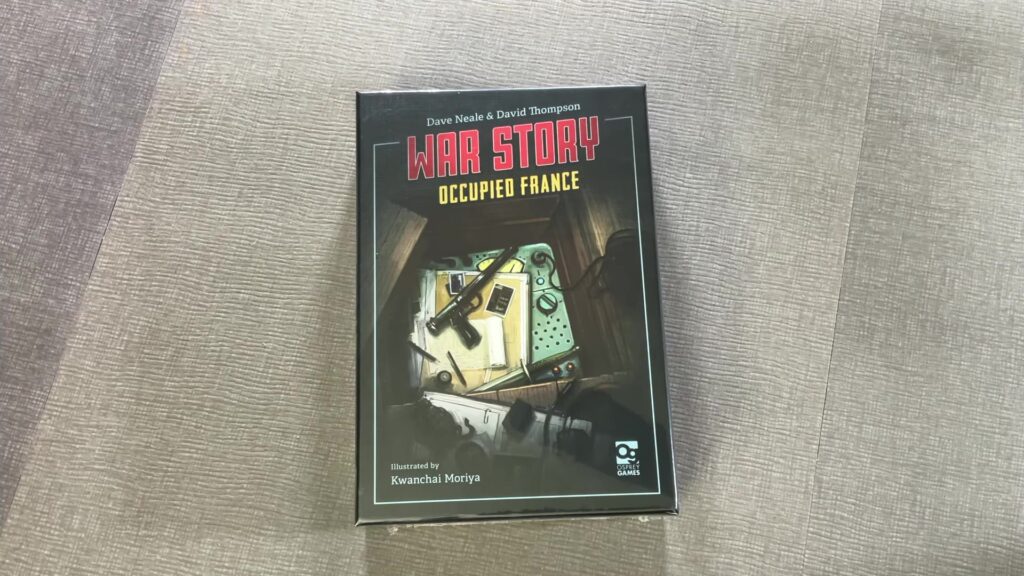 Box of the board game "War Story: Occupied France" on a textured surface, featuring a cluttered desk with wartime items.