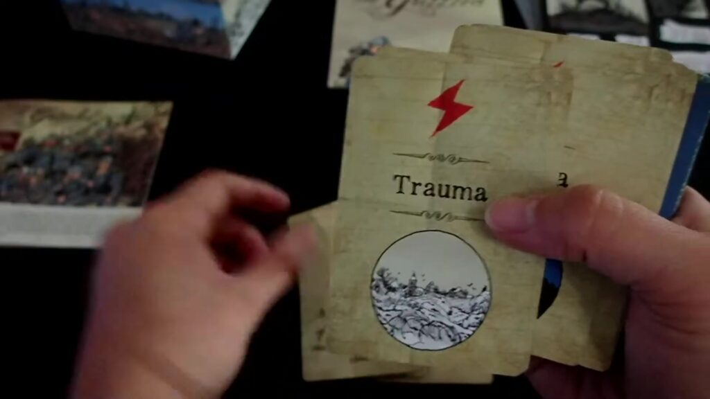 blue card with barbed wire art and two trauma cards with lightning bolt symbols and war-themed illustrations from the board game "The Grizzled."